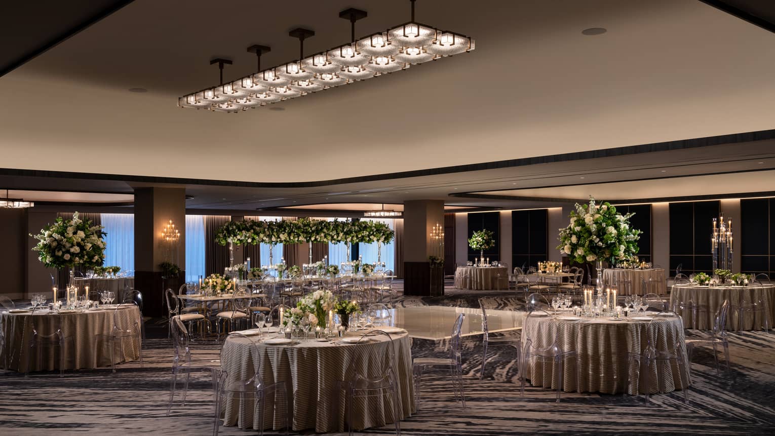 A ballroom with round tables and grey table clothes with flowers and plants as centerpieces on the tables.
