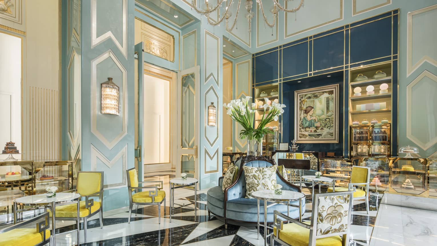 A tea room with tables arranged for two around the room; desserts displayed in glass casings along the walls