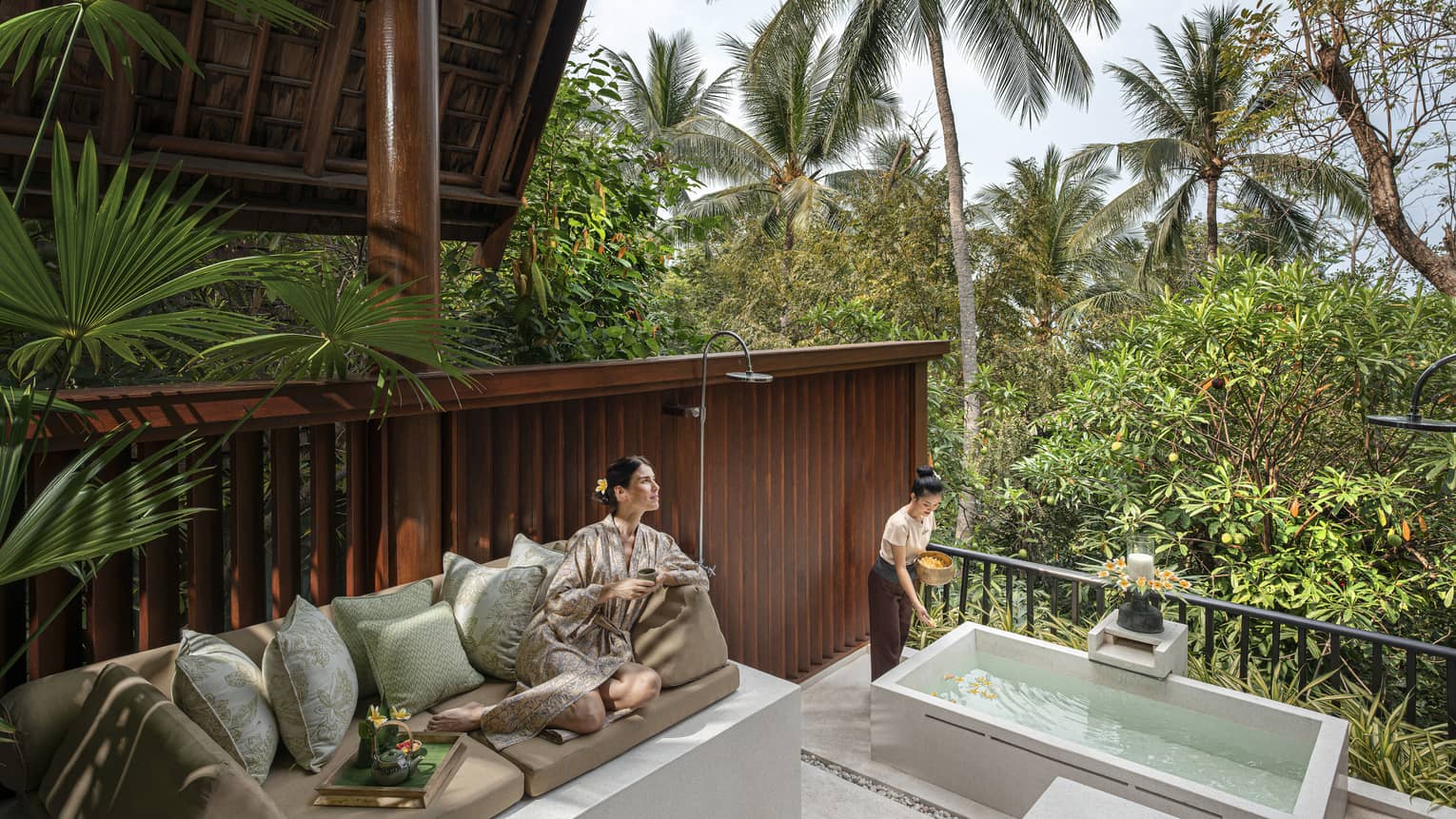 Woman in silk robe lounges on outdoor sofa at the resort spa amidst the lush green garden.