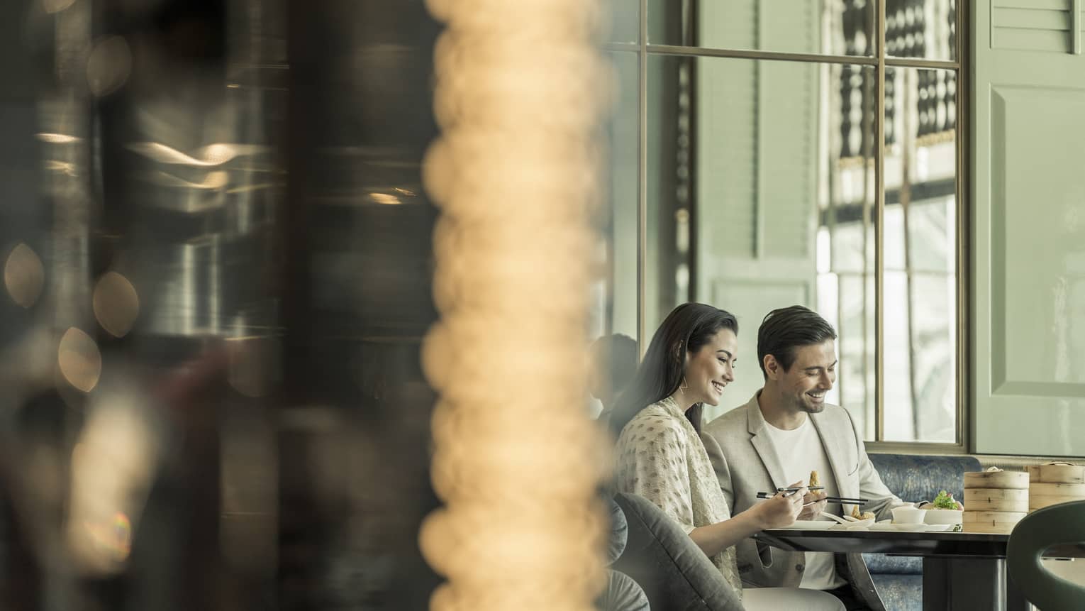 Man and woman sitting at table enjoying sushi with chopsticks