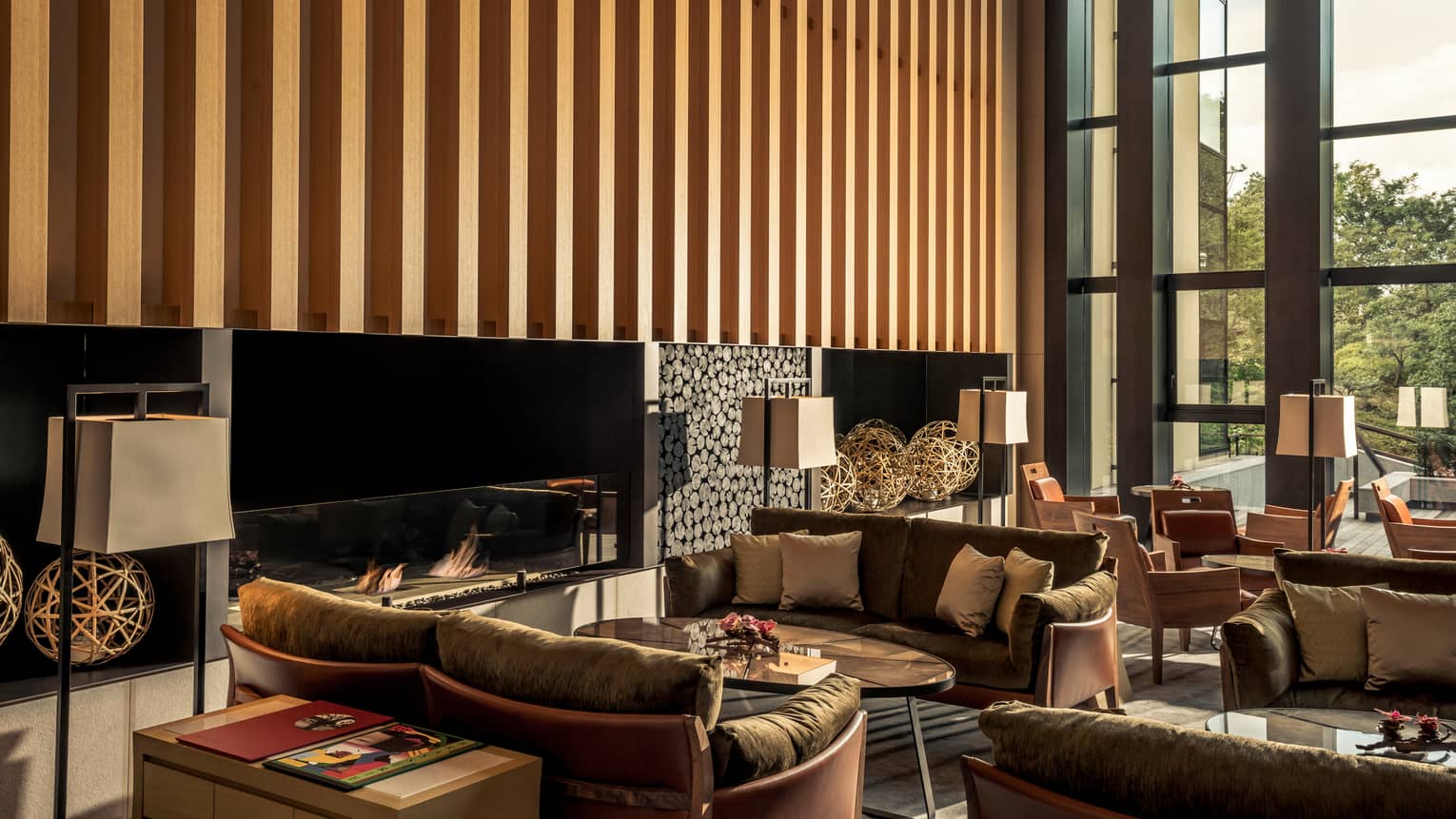 Brasserie brown loveseats, tables by modern fireplace under wood striped wall