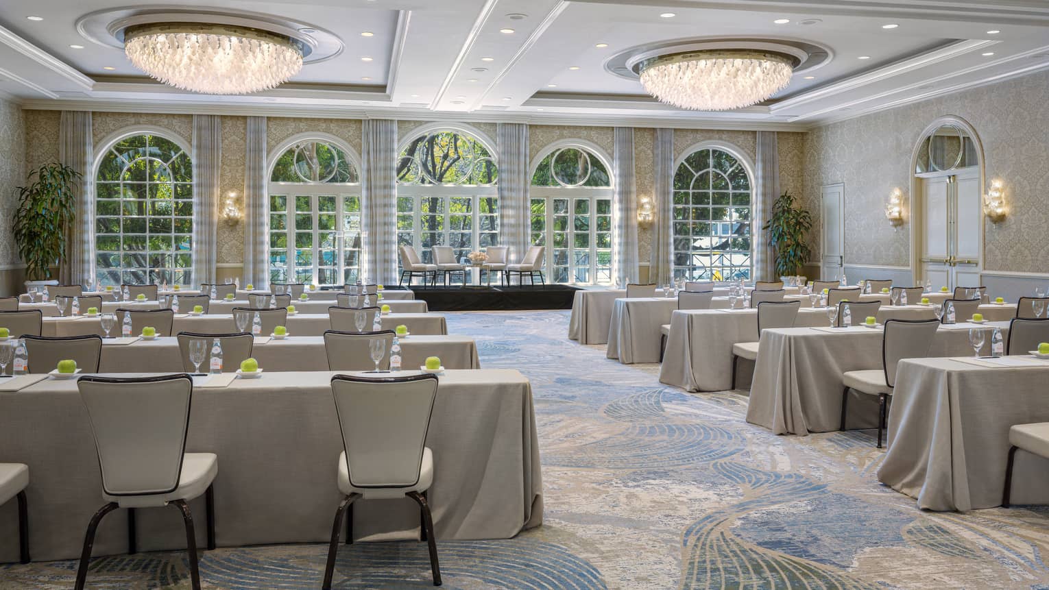 Ballroom set classroom style with cream-coloured linens, dual chandeliers, lighted wall sconces and floor-to-ceiling windows
