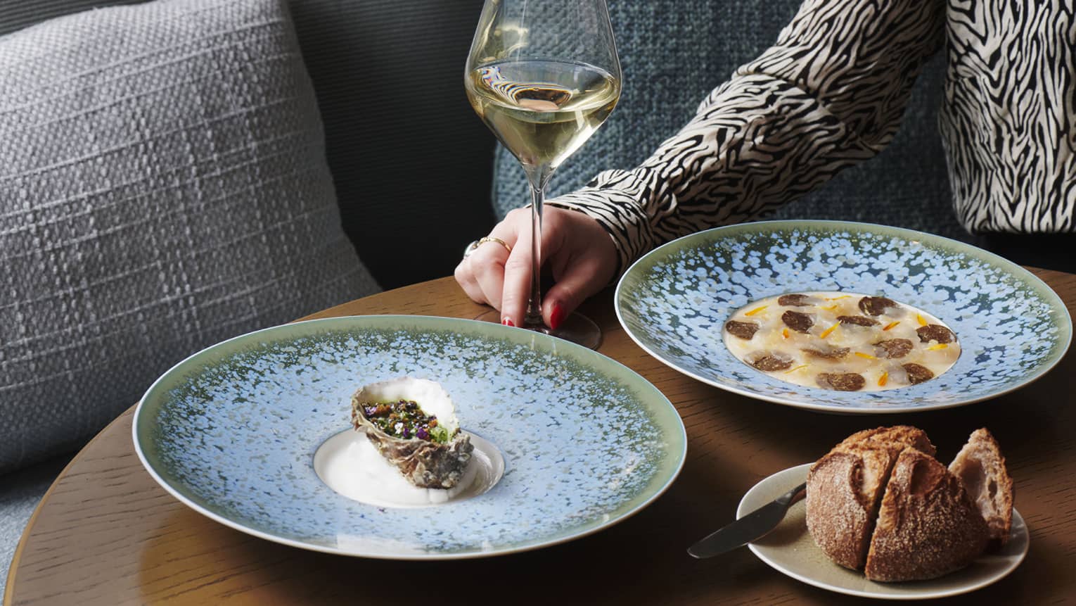 Blue plates with food next to a small plate of bread and a glass of wine.