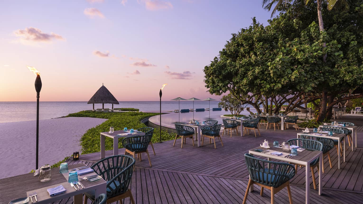 Tiki torches line the oceanside Reef Club terrace that's ready for guests with tables set with plates, silverware, blue napkins, all overlooking the ocean