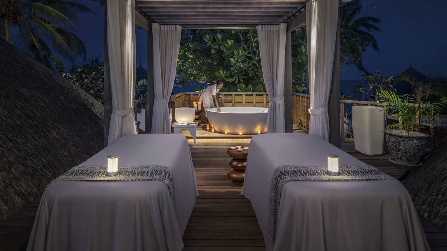 Couples massage beds with glowing candles at outdoor spa pavillion at night