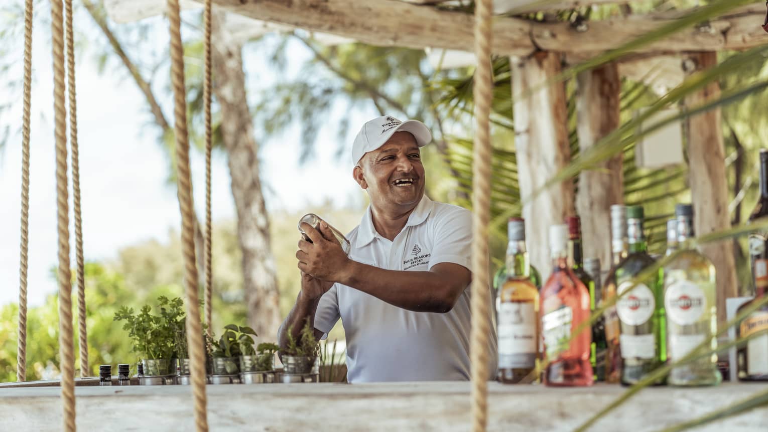 A smiling bartender in a ball cap shakes up a cocktail