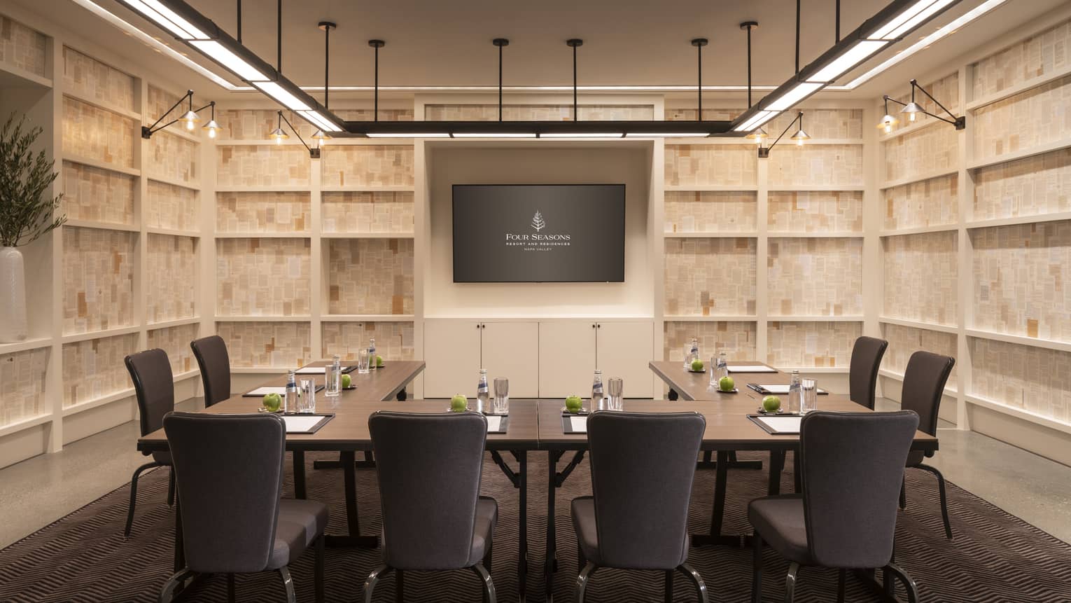 Private meeting room with light wood walls, TV screen on wall, l-shaped table