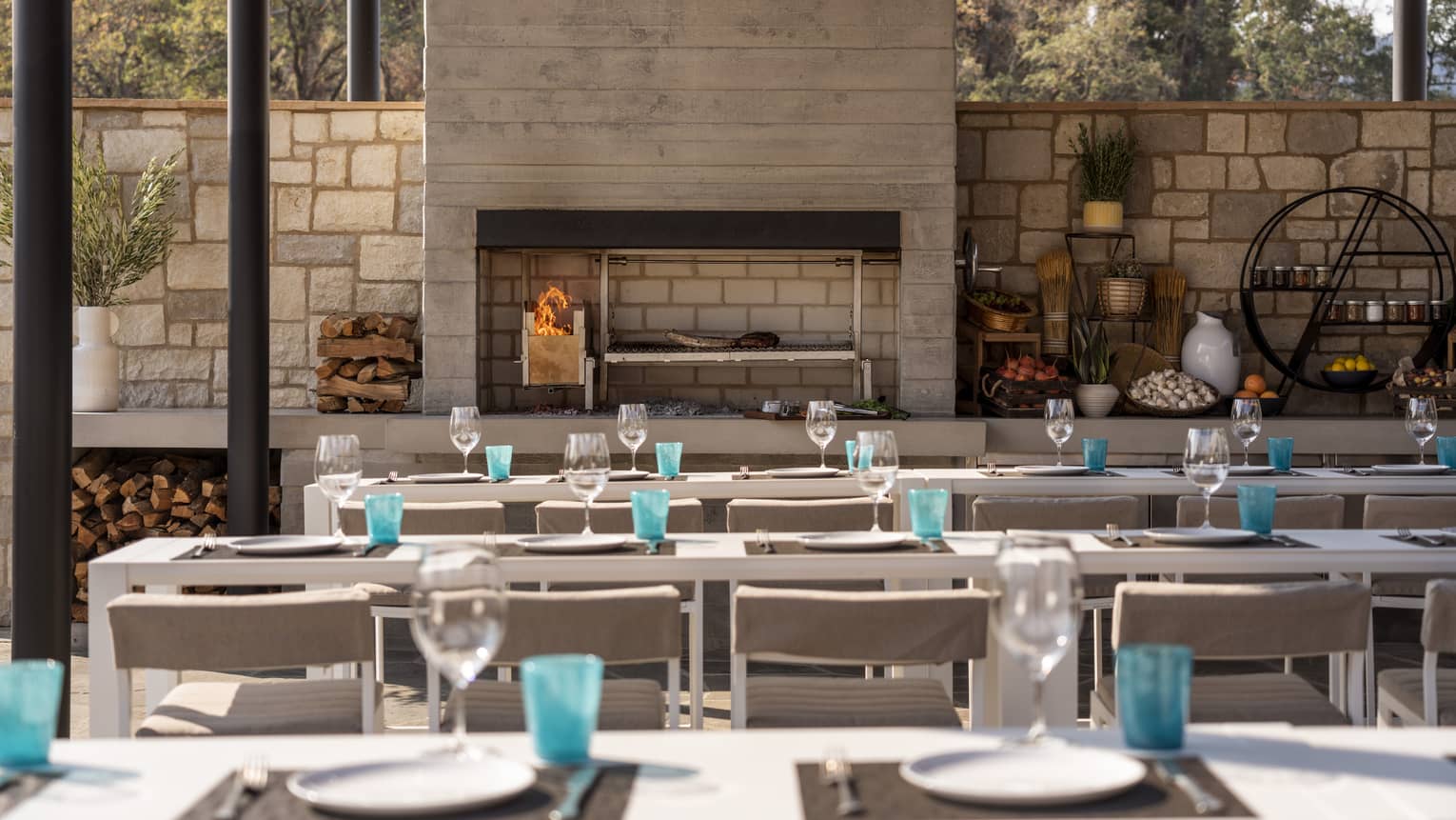 Rows of tables outside near a fire place and a stone wall.