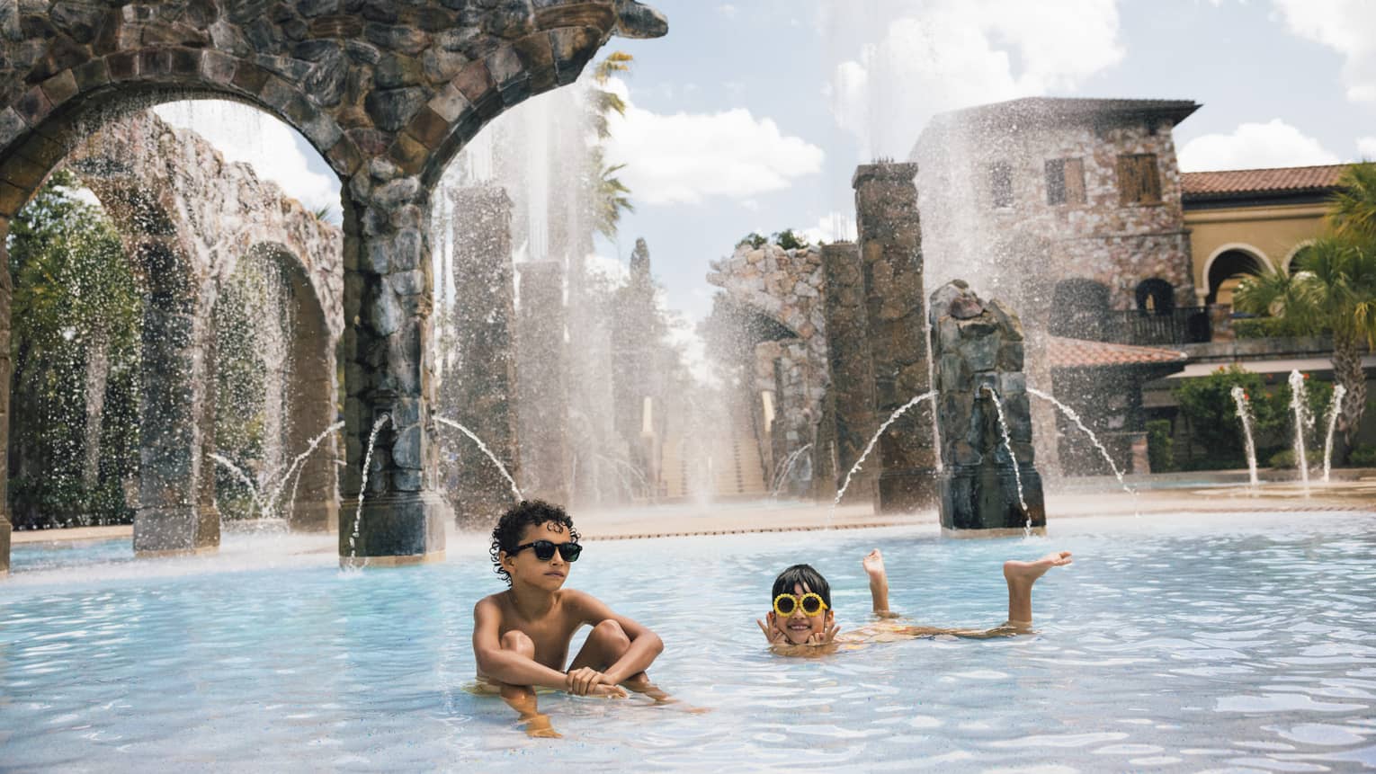 Two young guests wearing sunglasses and swimming in an outdoor water park pool.