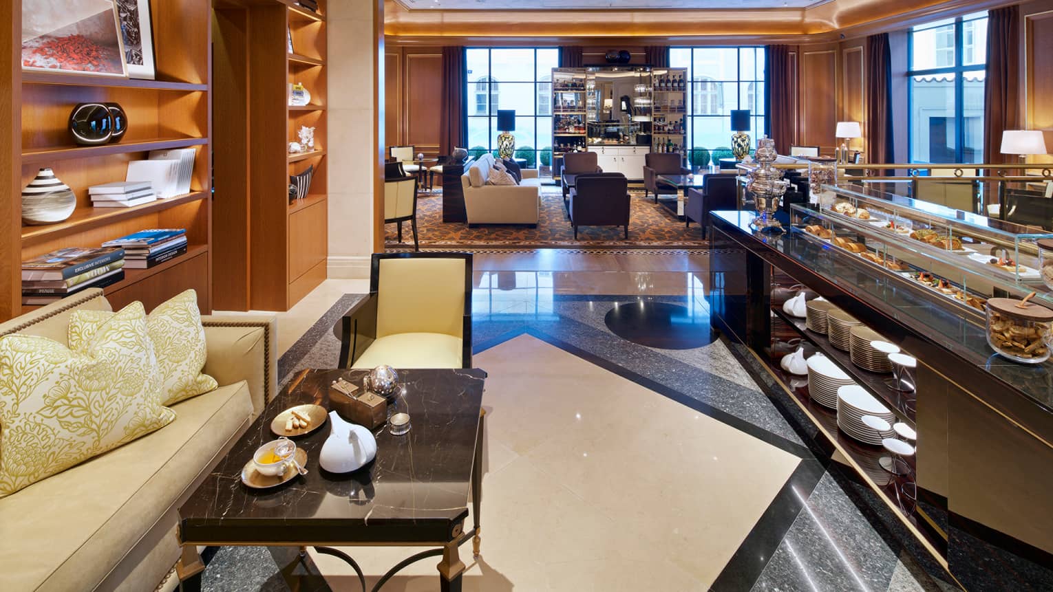 Cafe bakery counter with desserts in glass display across from small sofa, table with teapot, cup and cookies