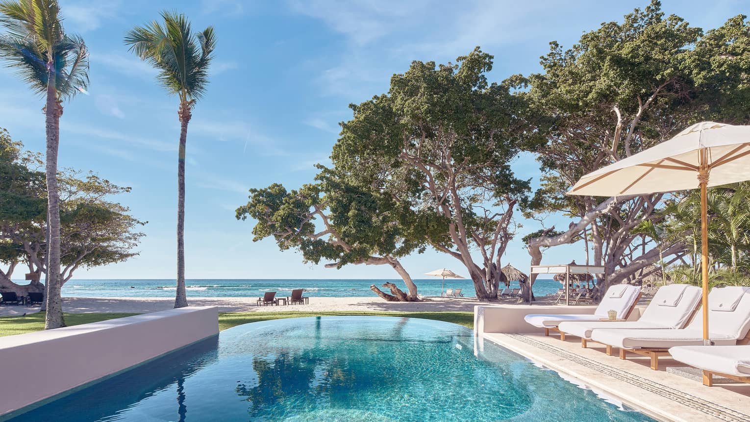 Arena Beach House pool with white lounge chairs, umbrella, palm trees, ocean views