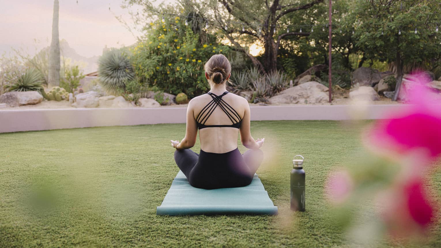 Person doing yoga outside on a blue yoga mat with a water bottle beside them.
