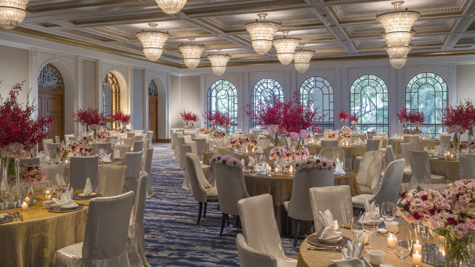 Circular tables are set for a meal and decorated with candles and pink and red bouquets