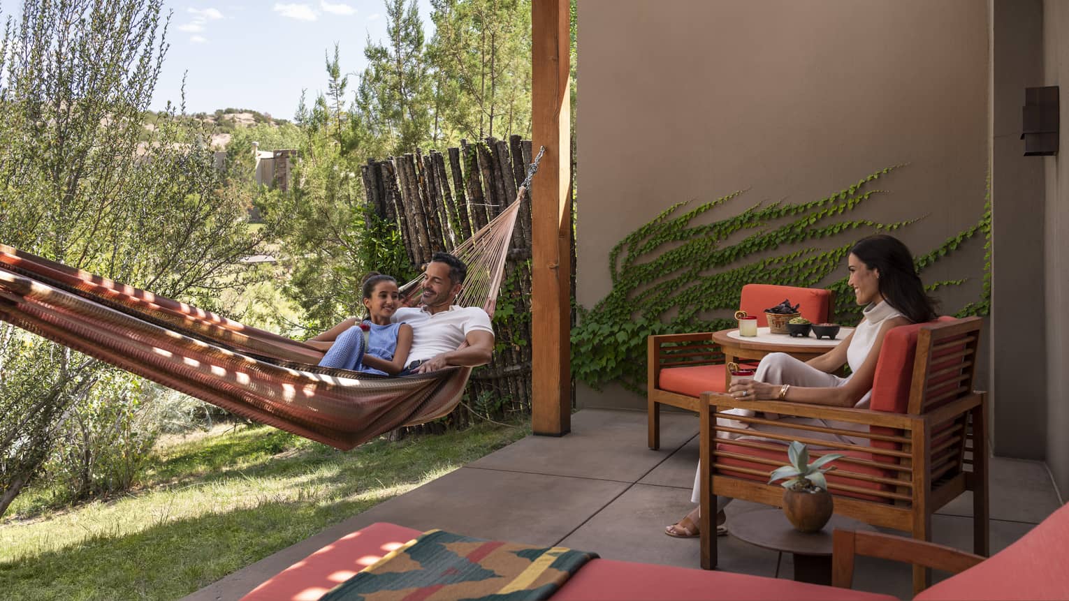 A family sitting on a chair and hammock outside near plants.