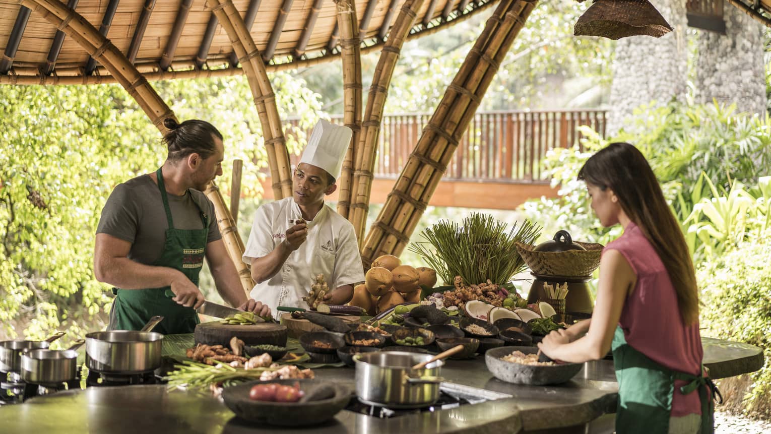 A four season chef instruction a man and woman how to cook in an outdoor kitchen