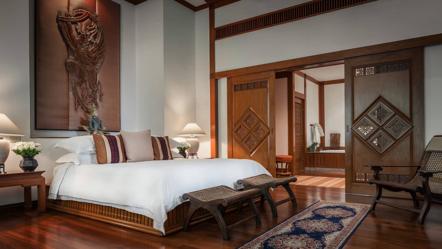 Spacious bedroom with a large bed, wooden furniture, carved sliding doors, decorative cushions and traditional artwork on the wall