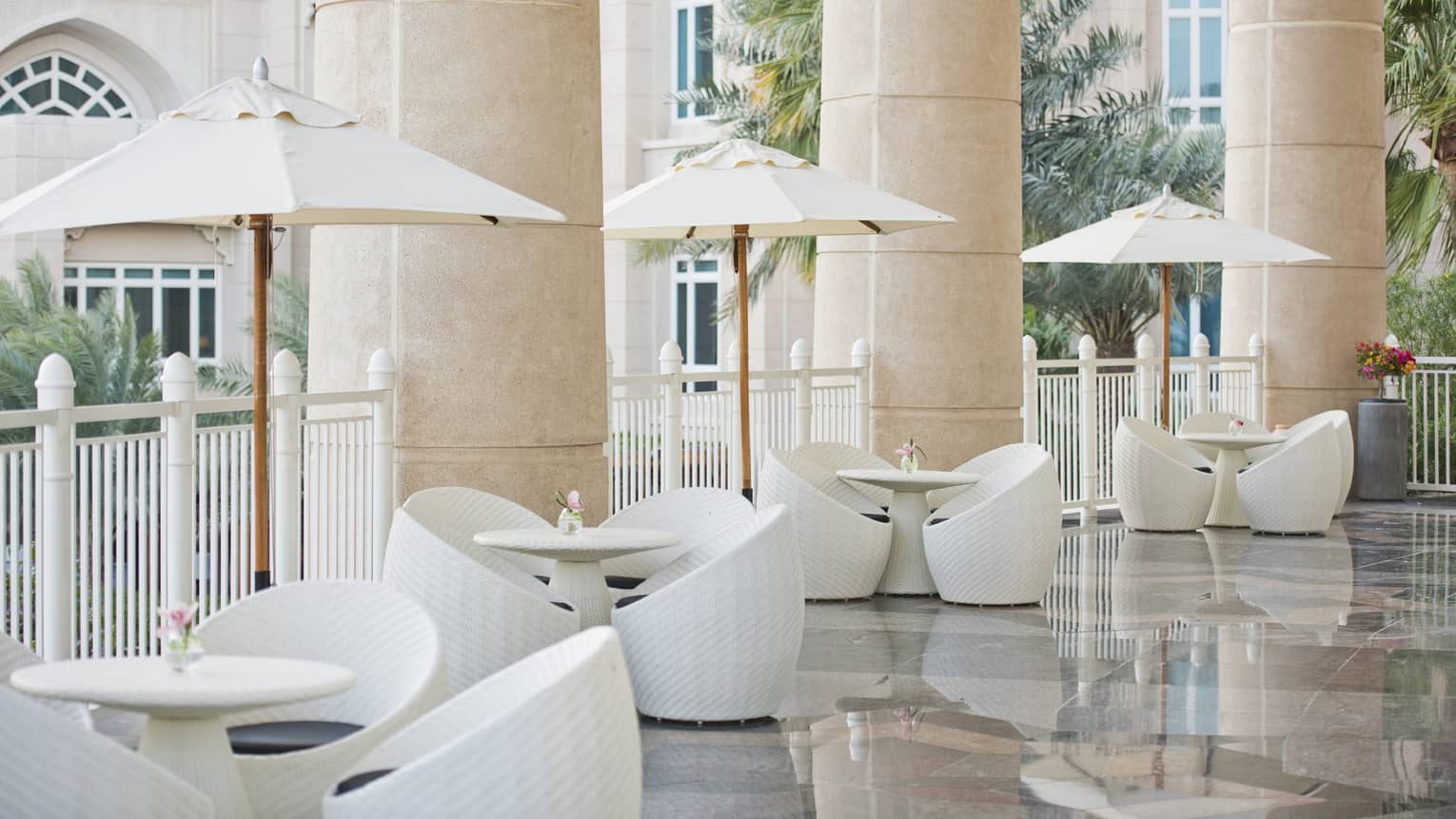 White tables and chairs set under white umbrellas line an outdoor terrace