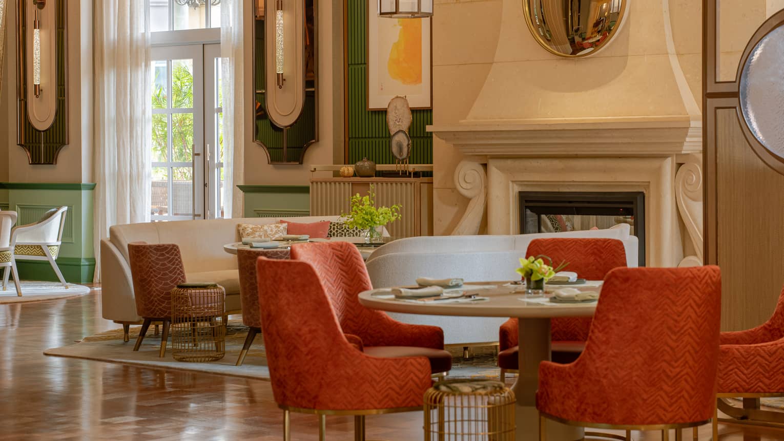Hotel lobby lounge area with burnt-orange seats, round table, windows, large fireplace