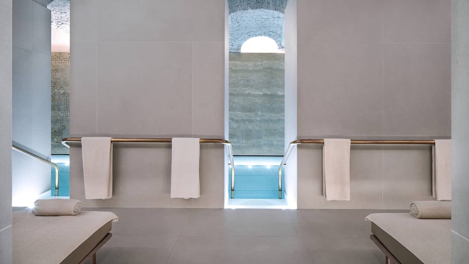 Concrete spa pool deck with white spa loungers, white towels hanging and pool entry between tall white walls