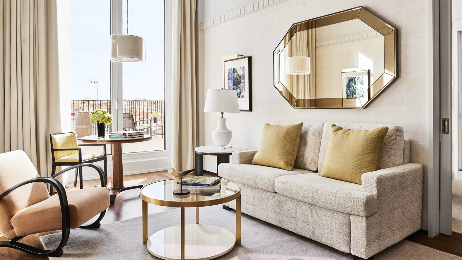 Four Seasons suite living area with a beige sofa, round tables, chairs, octagonal wall mirror and terrace