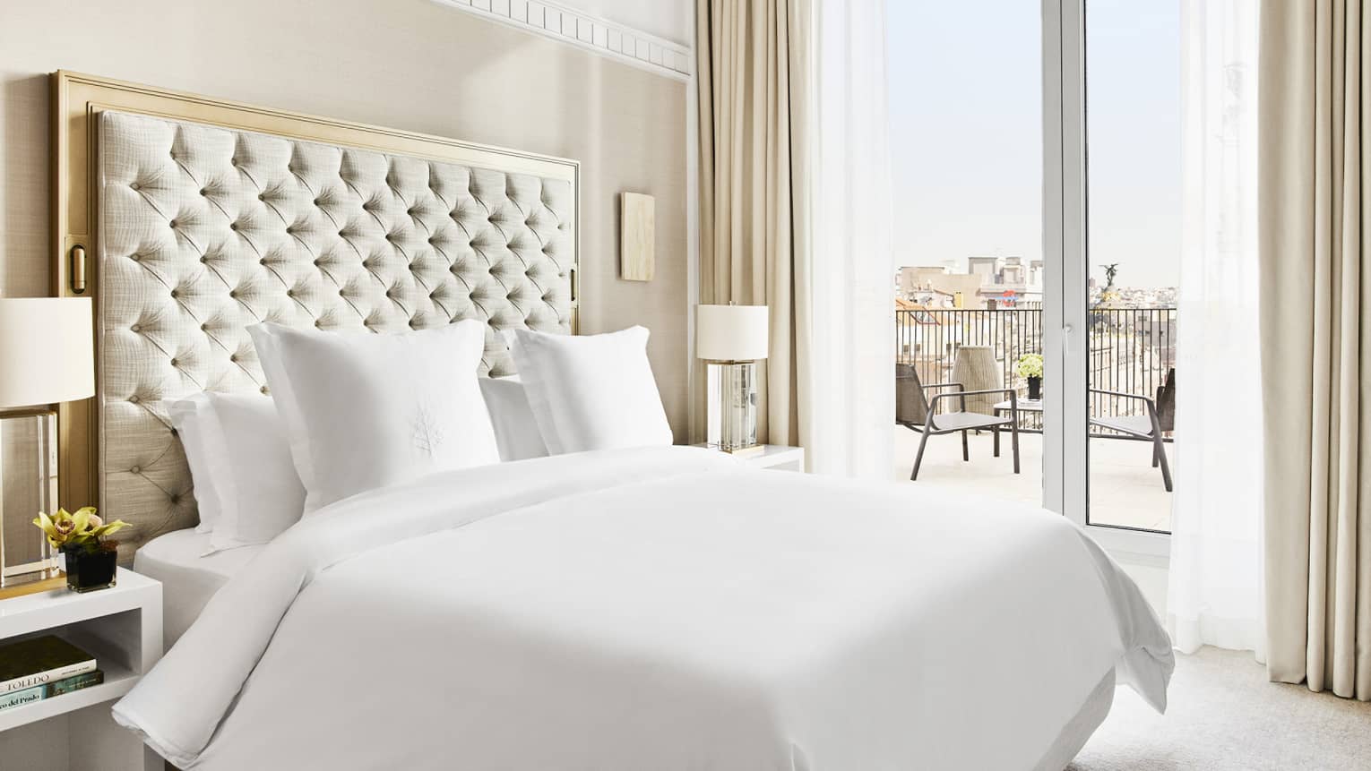 Luxury hotel suite bedroom with a king bed, tufted headboard, bedside lamps and access to a private terrace with city views