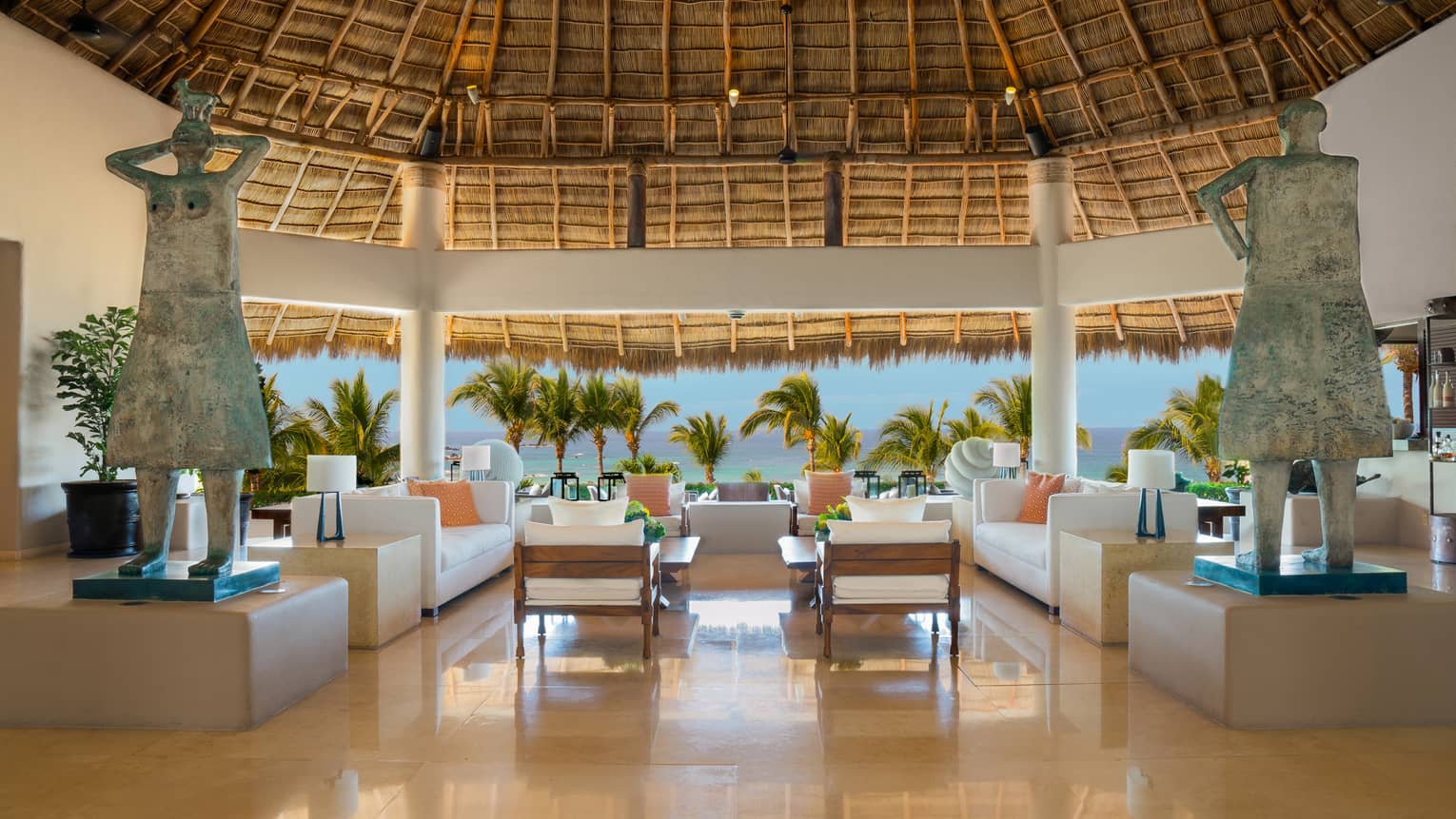 Indoor-outdoor lobby area with two sofas and two arm chairs under thatched-roof ceiling