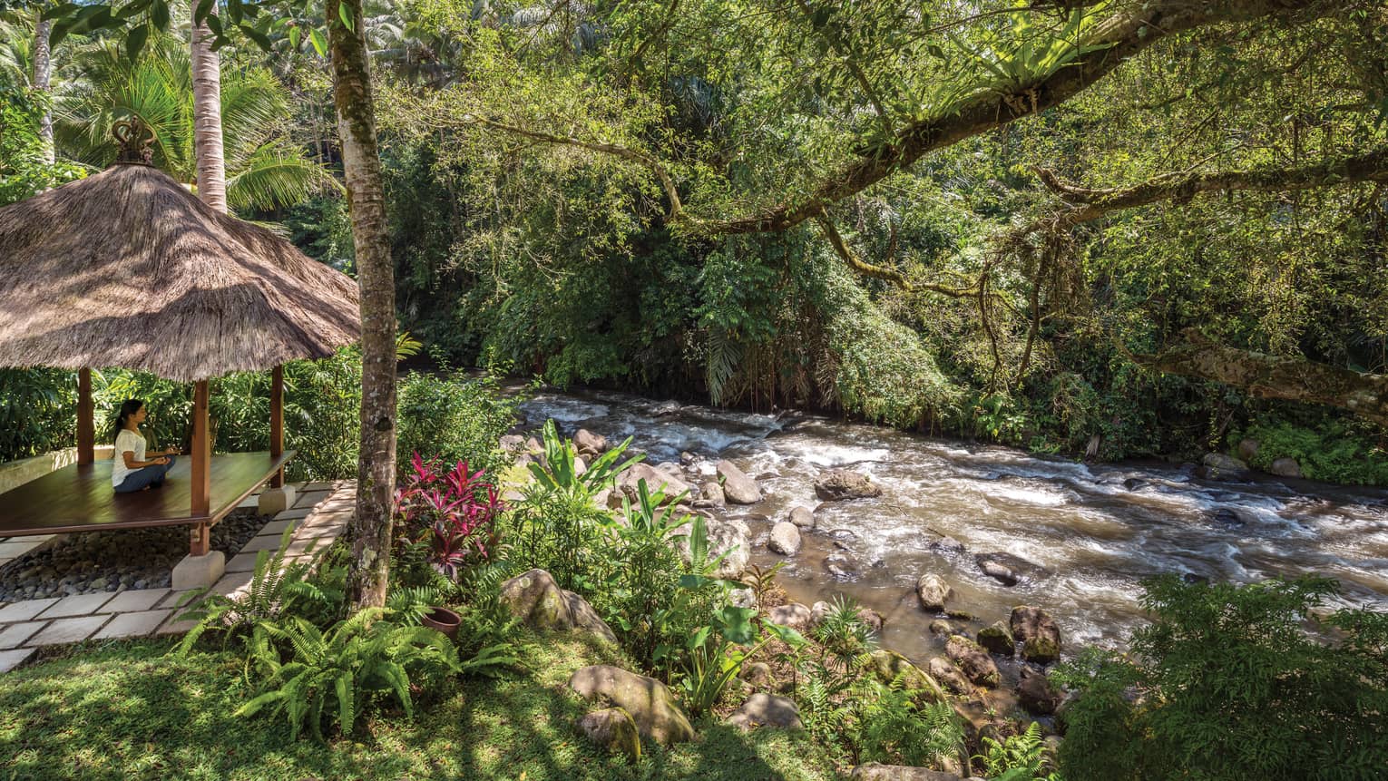 A guest meditating in a pavilion next to a flowing river in Bali