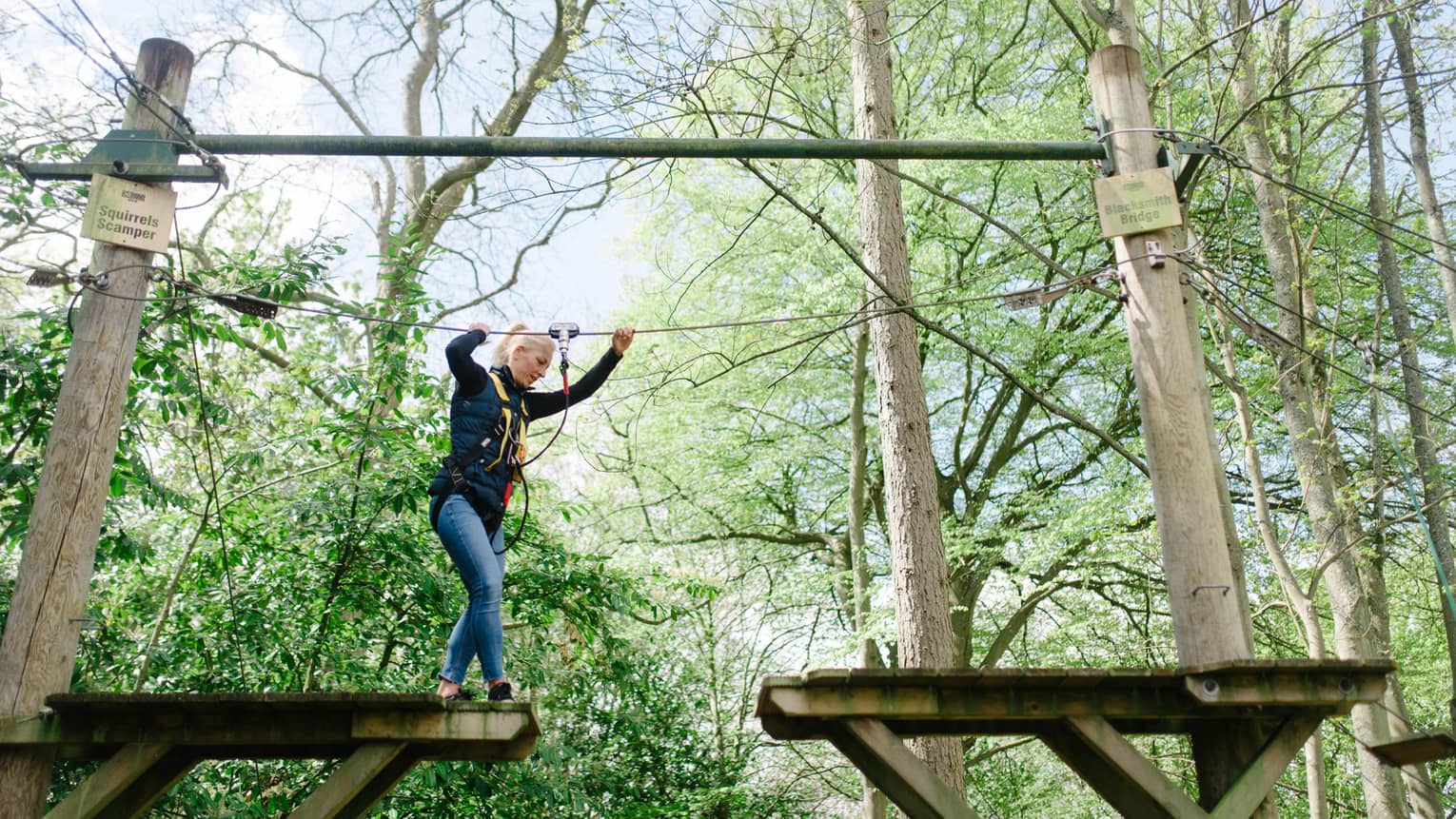 Woman traverses highwire ropes course in woods while tethered