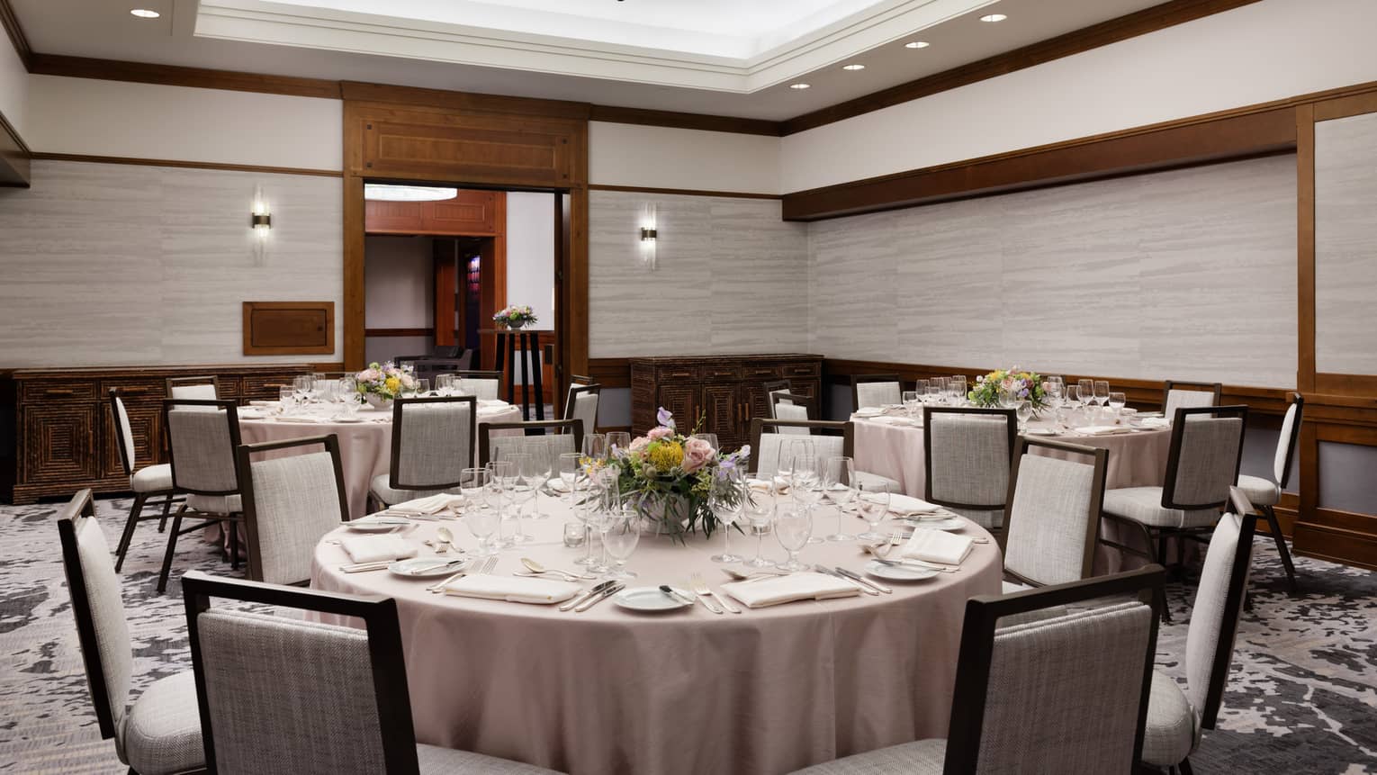 A room with large round tables with table cloths and grey chairs.