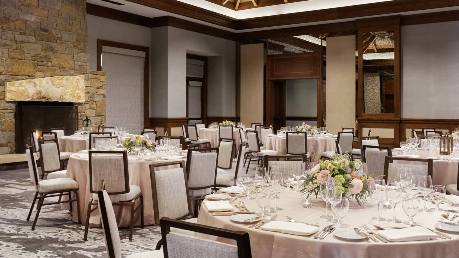 A large room with wood details, round tables with table cloths and grey chairs.