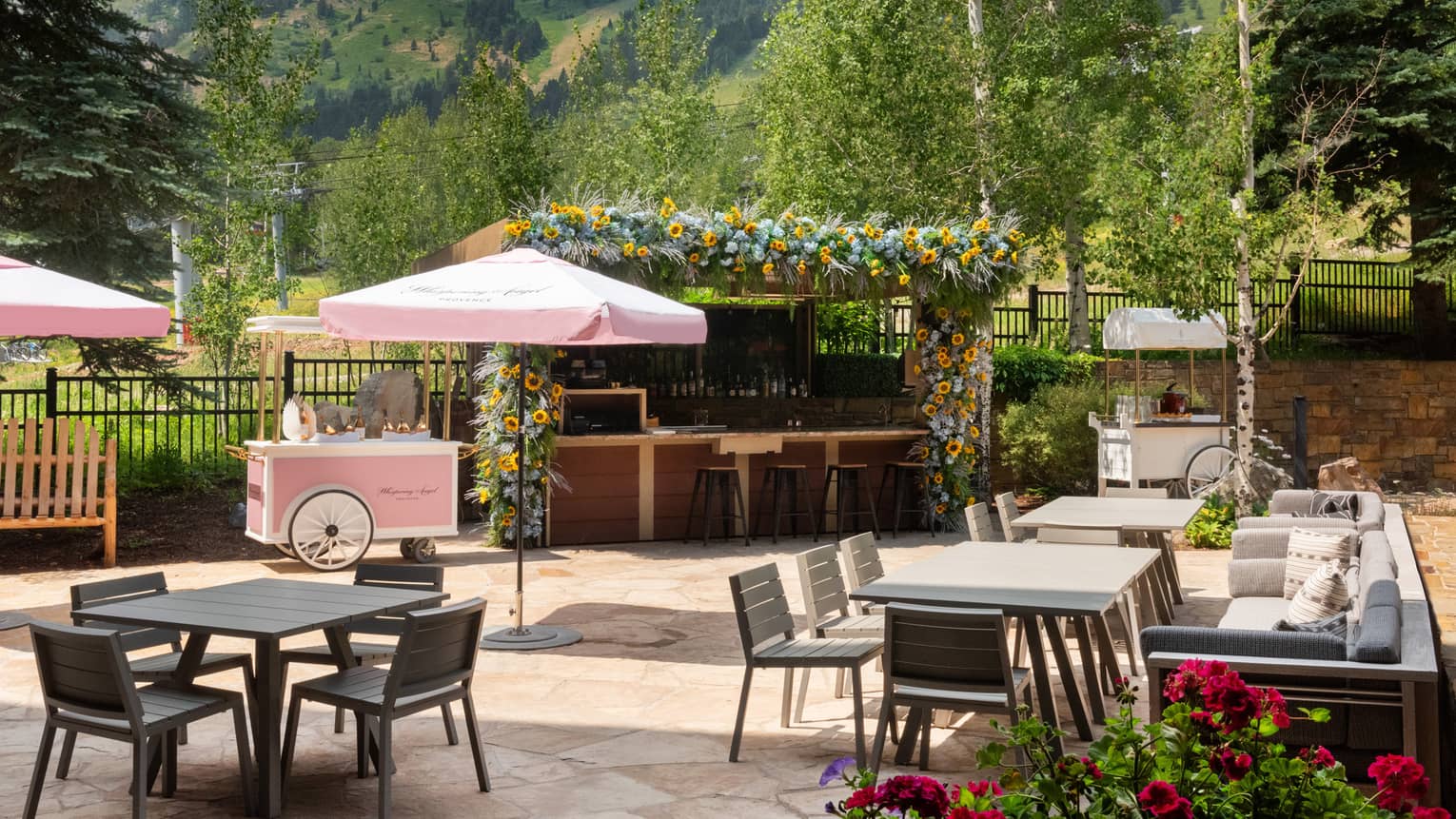 Outdoor patio with seating areas with pink umbrellas, a view of the mountains in the background.