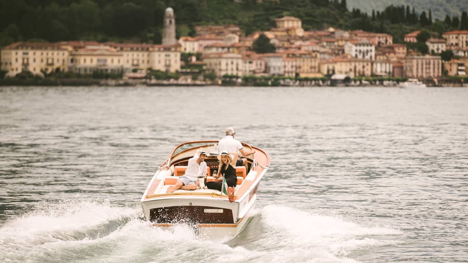 Couple laugh, drink Champagne on back of powerboat on Lake Como