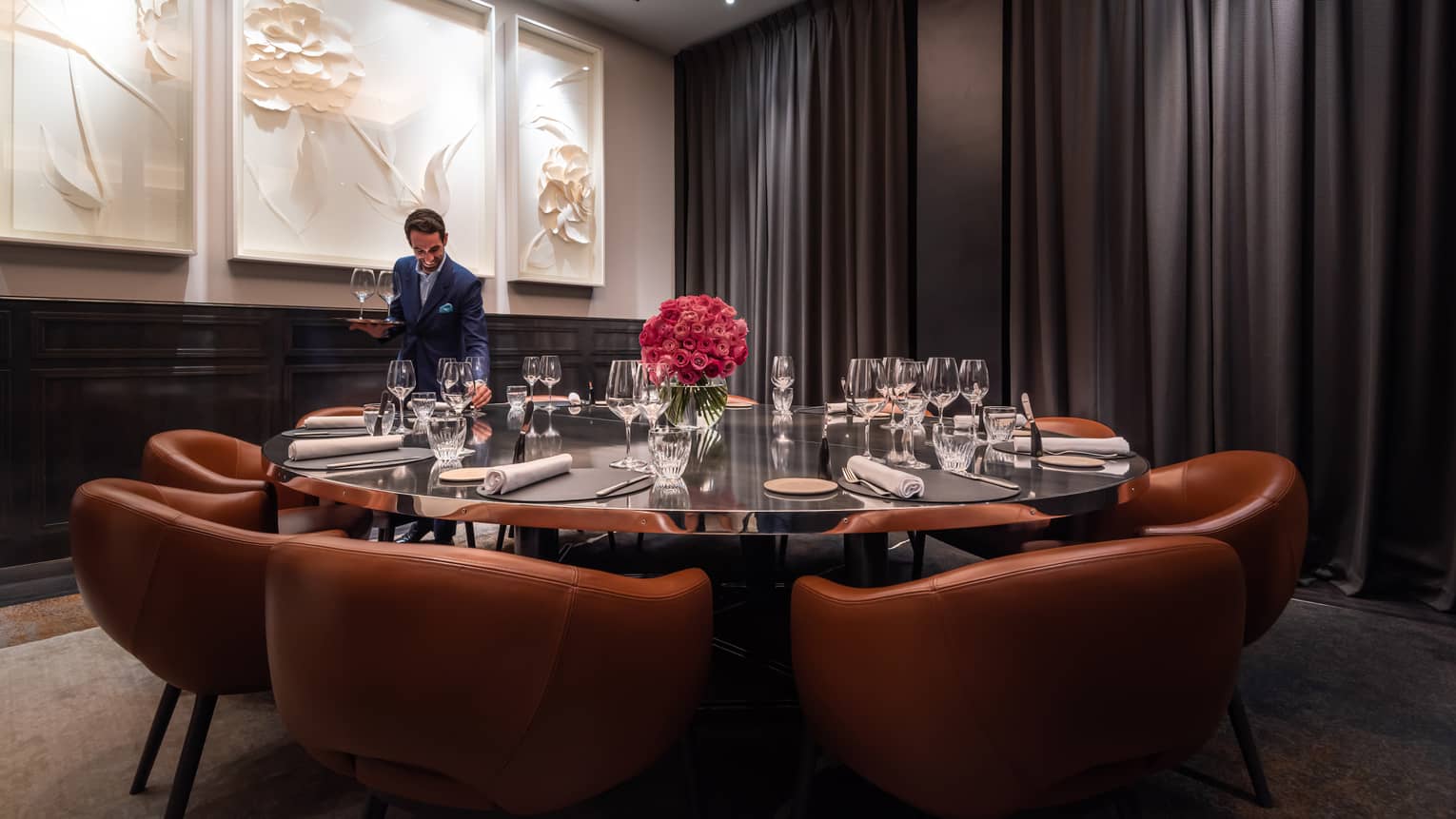 A large round table with leather chairs and a team member placing table settings.
