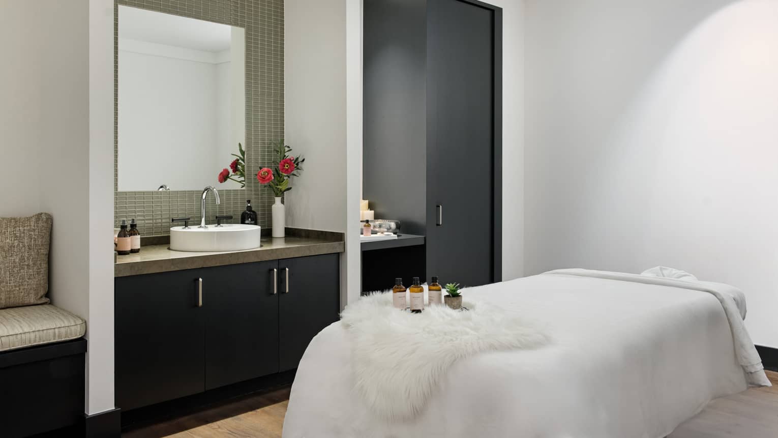 Spa room with massage table, sink with a vase of flowers on it, and cabinets.