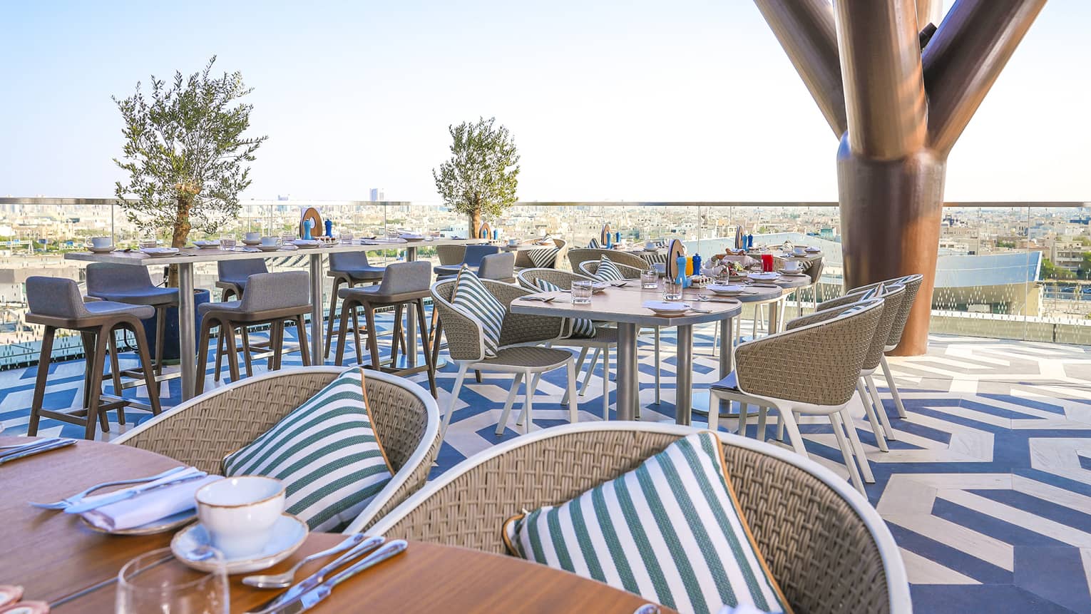 Elements' outdoor patio outfitted with rattan chairs, wood tables and a blue-and-white patterned floor, all overlooking the park with the city in the distance