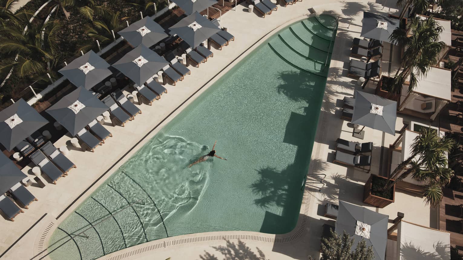 Aerial view of an outdoor pool surrounded by grey lounge chairs and umbrellas, creating a relaxing atmosphere.