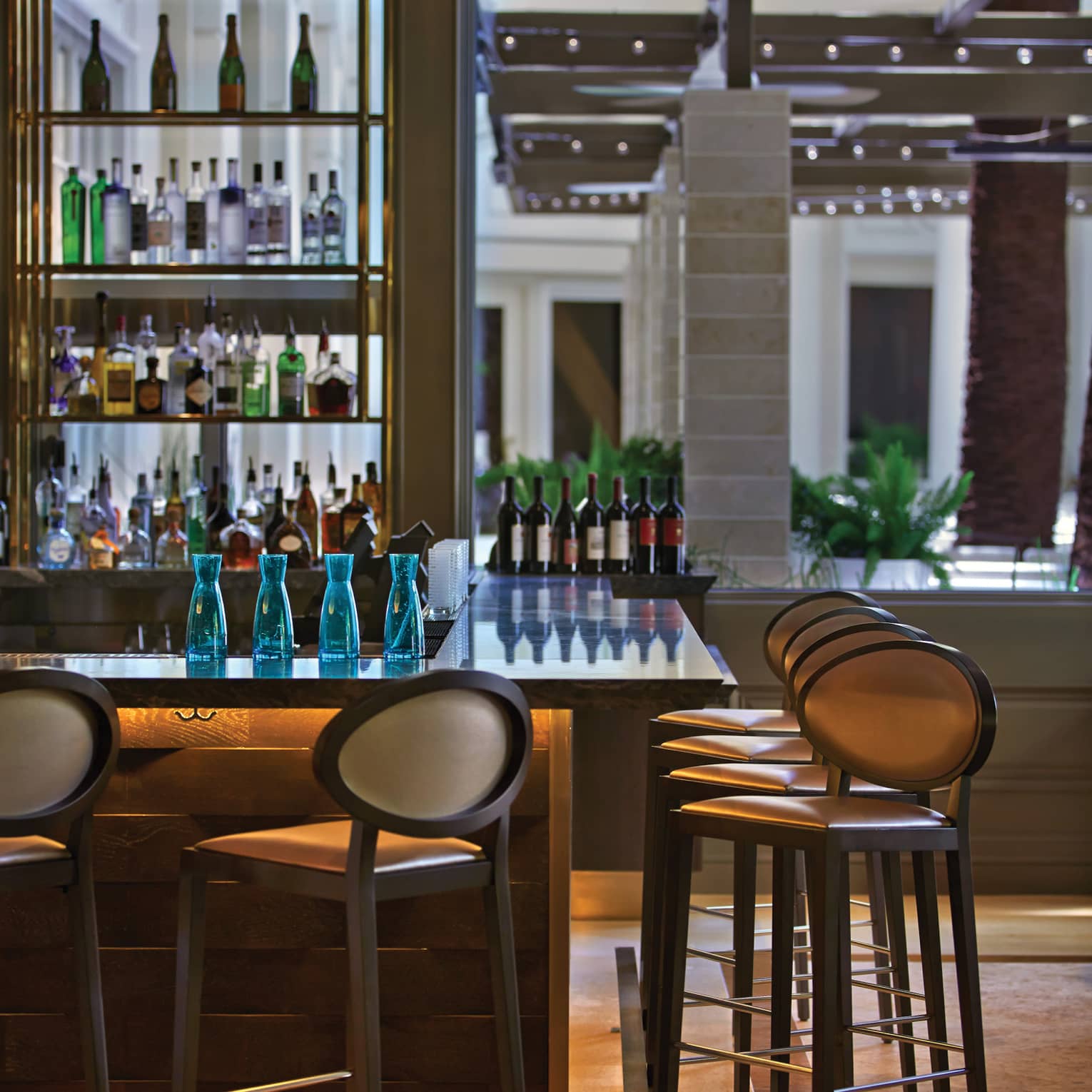 Tall chairs line a bar counter, bottles of wine and spirits arranged along the counter's far edge and on shelves behind.