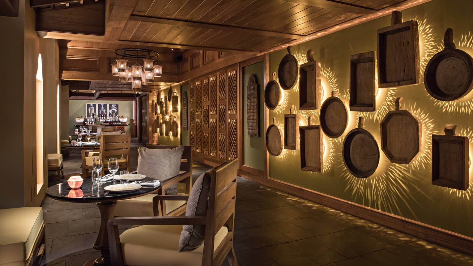 Dimly-lit KHAO indoor dining room with tables across from decorative brass wall with lights