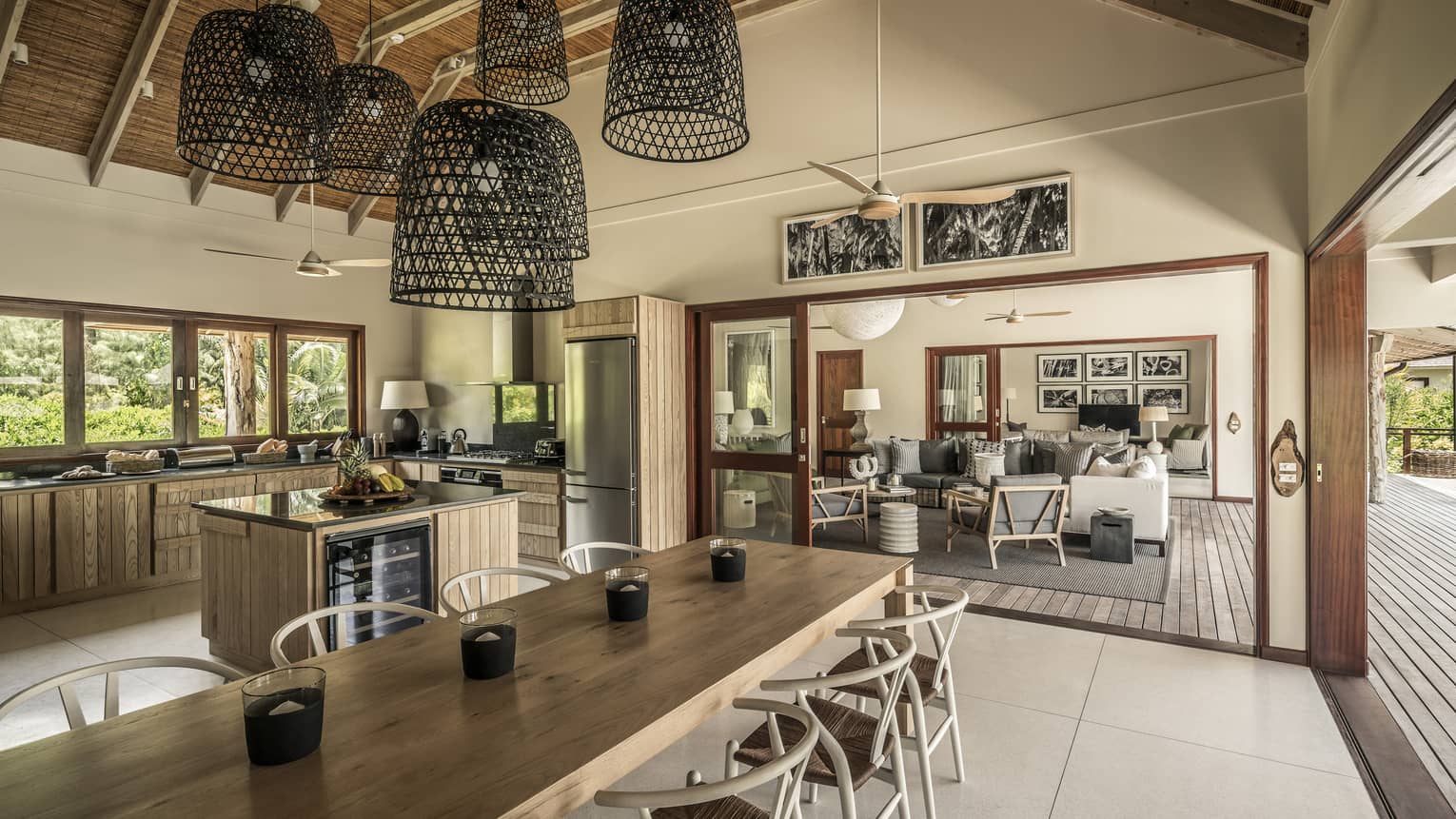 Large basket-like chandeliers hang from gambrel roof over long wood dining table, large kitchen