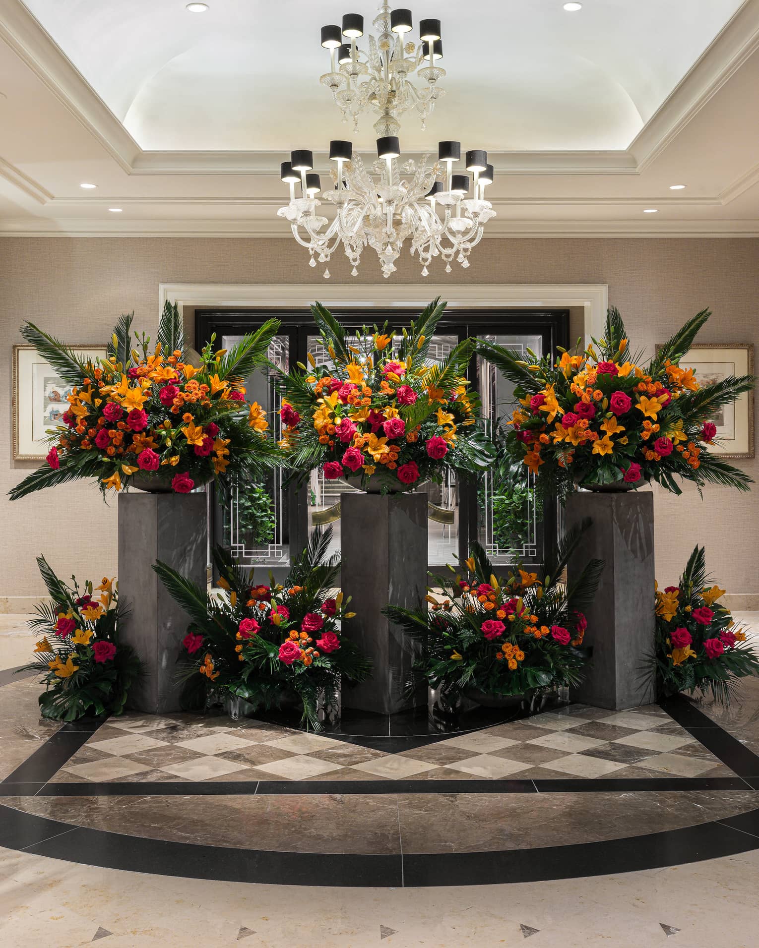 A bright, spacious, neutral-toned lobby area is decorated with elegant, artistic floral arrangements of red, orange and green.