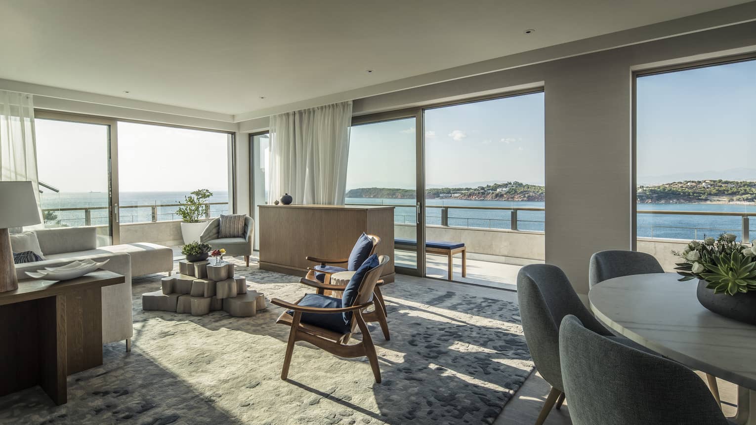 Arion Presidential Suite living area with white sectional sofa, navy arm chairs, dining table, panoramic views of Mediterranean Sea