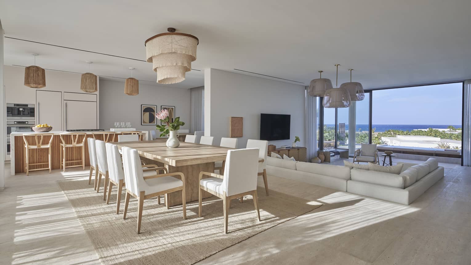 Modern open living area with dining table and white chairs, kitchen with barstools and sunken sectional facing tall windows and water view