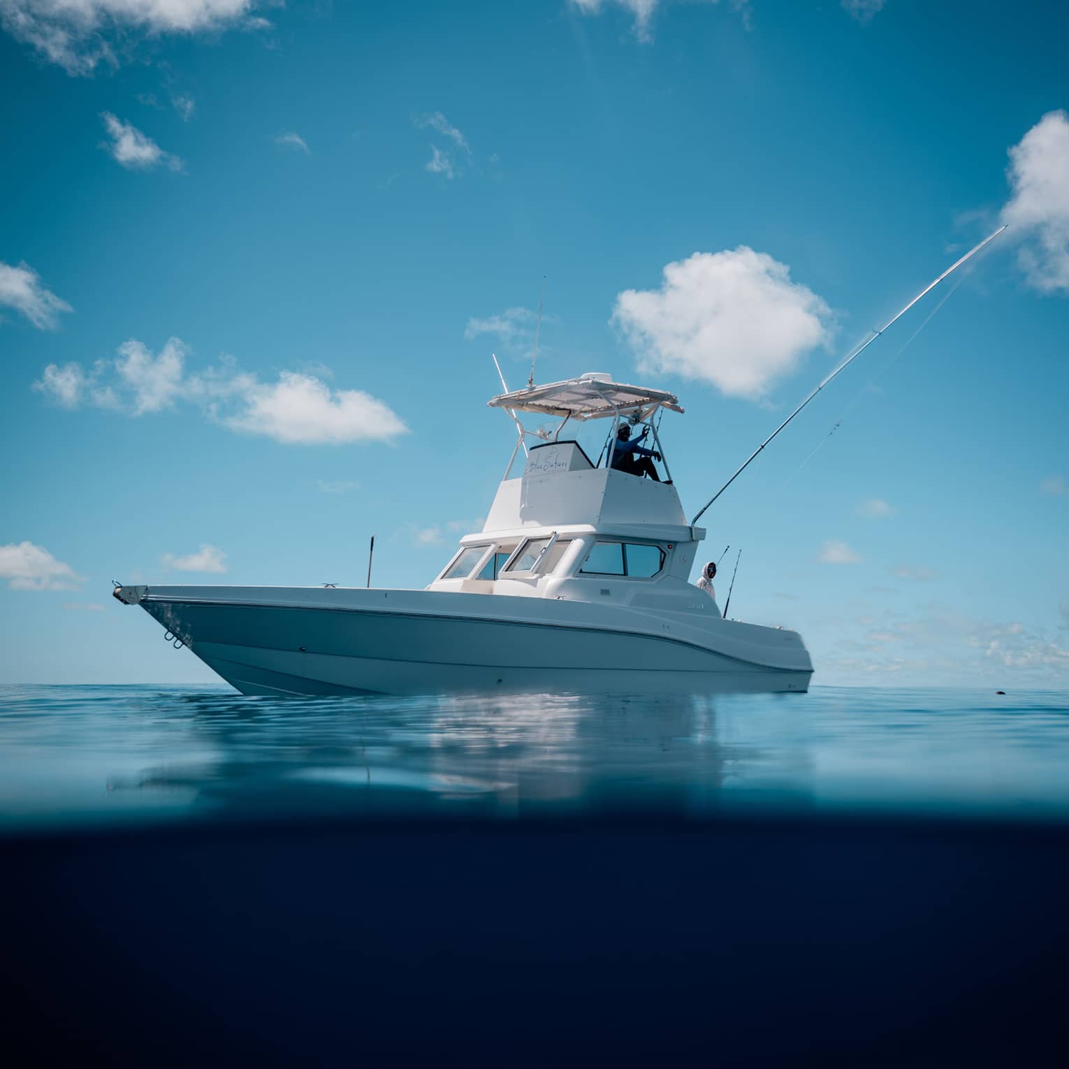 Under clear blue skies, two people aboard a centre console fishing boat; the boat's image reflected in the still water below.