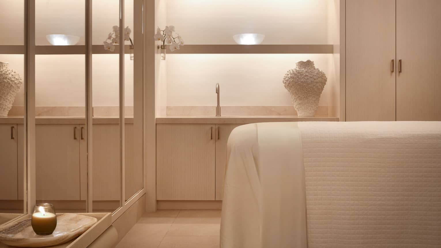 Spa treatment room bed with white linens across from mirror wall