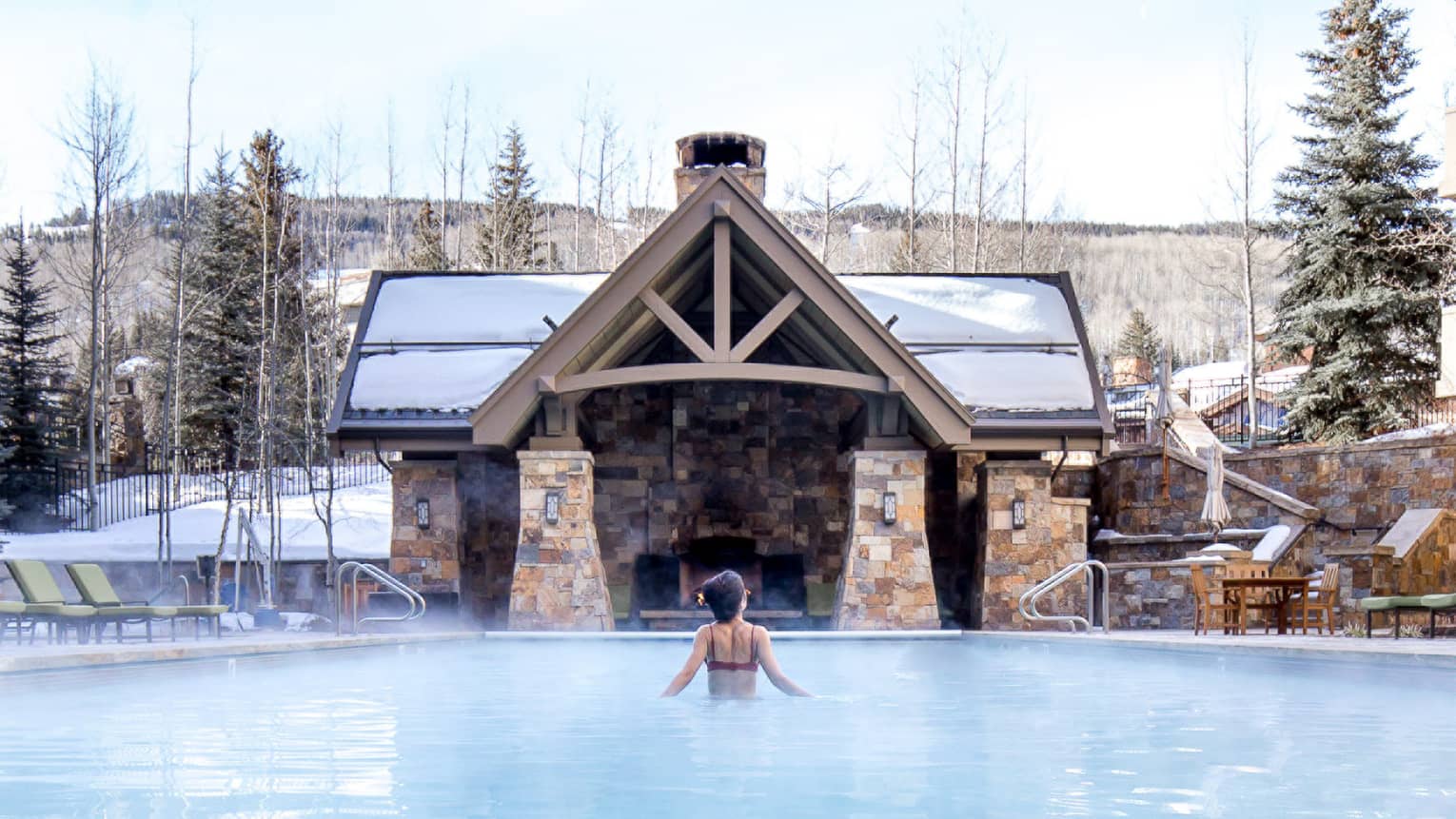A woman in a pool with trees covered in snow around her.