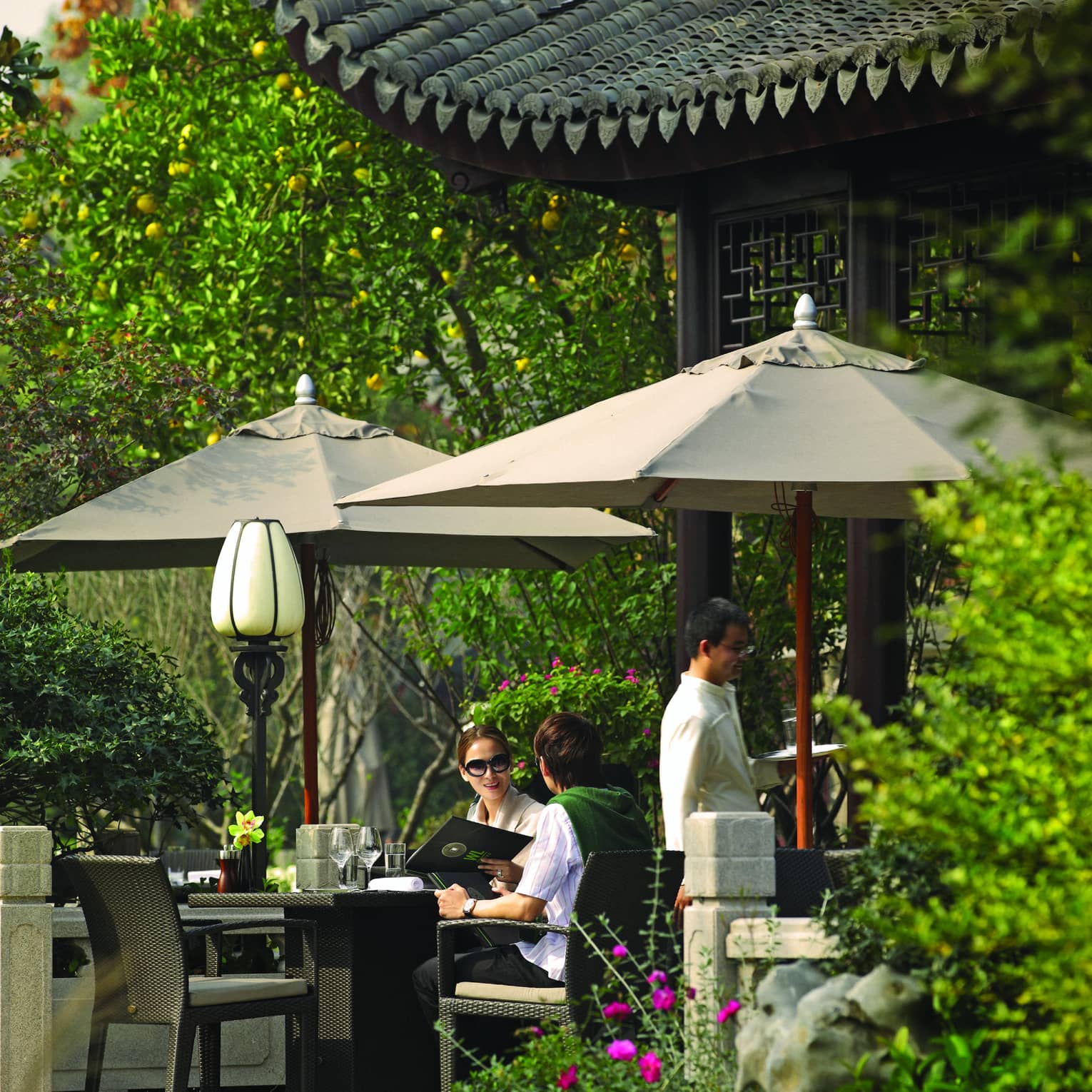 Couple holds menu at patio dining table under umbrellas, pavilion