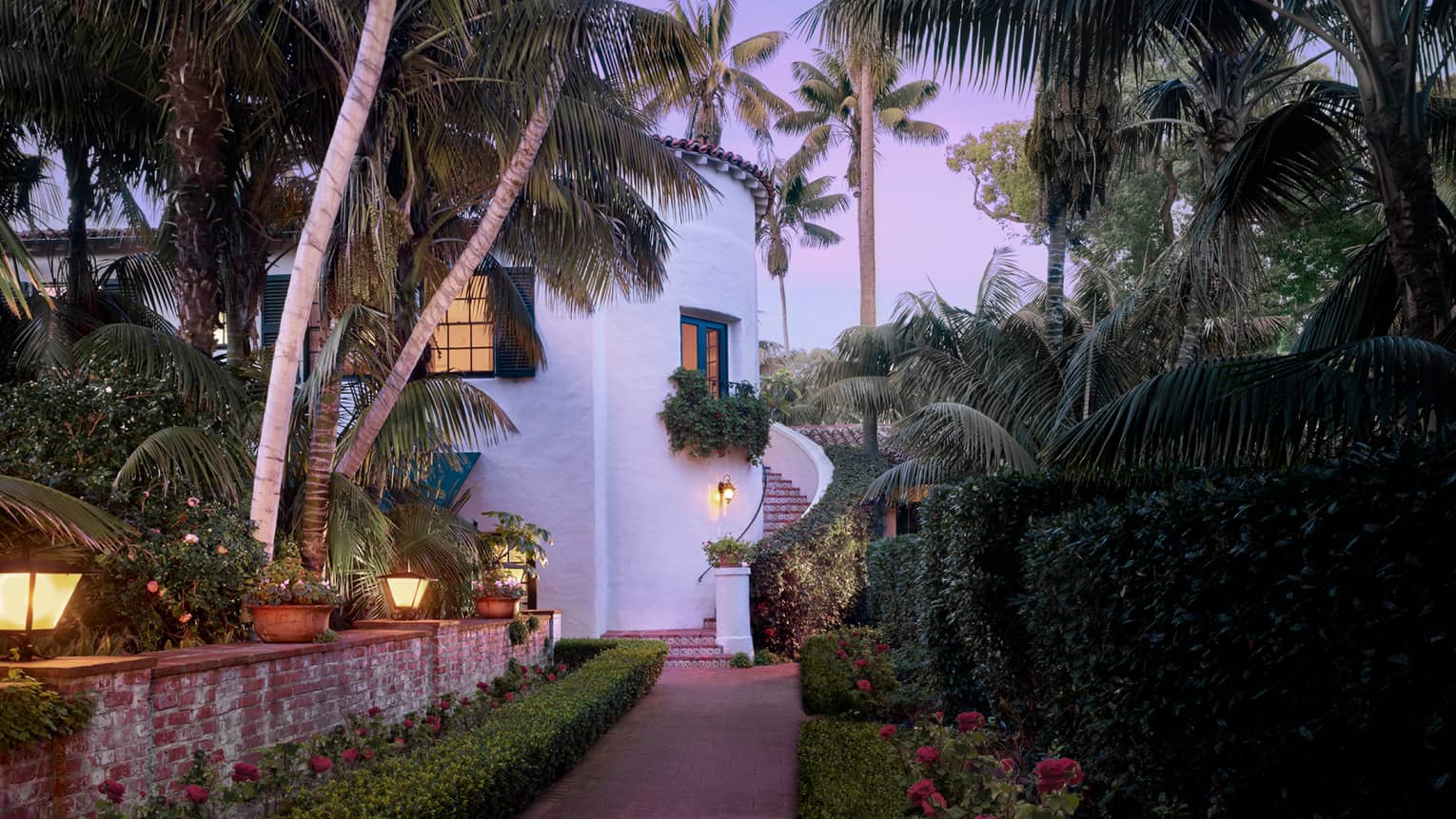 White concrete Honeymoon Suite with winding outdoor staircase by garden path under palms