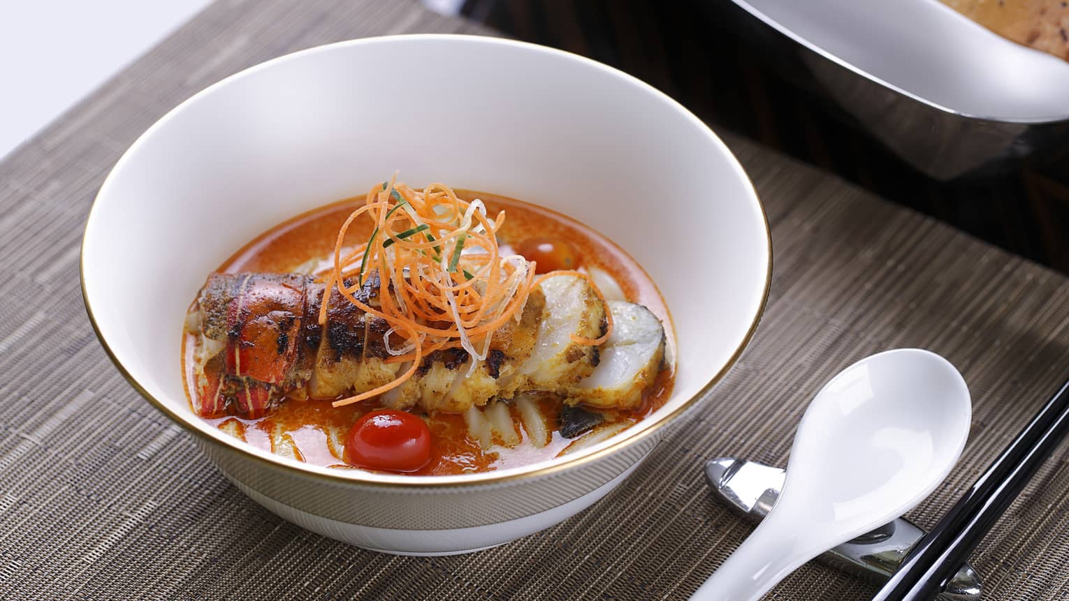 Bowl with lobster in red sauce, carrot garnish