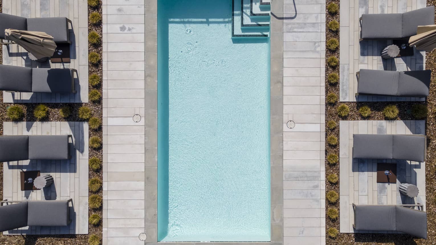 Aerial view of a rectangular pool, four grey lounge chairs on either side