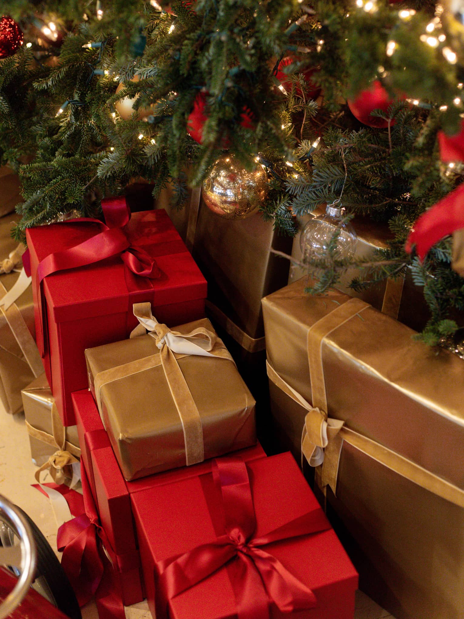 Close-up of red and gold gift boxes with bows under a Christmas tree decorated with red and gold ornaments.